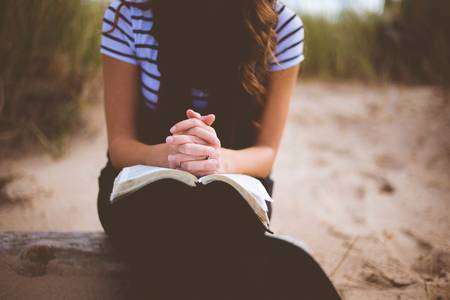 Quelle: pixabay.de / StockSnap, https://pixabay.com/de/photos/menschen-m%c3%a4dchen-allein-sitzung-2604834/ Frau betet über einem Buch im Sitzen
